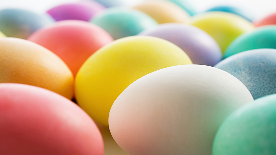 A vibrant collection of Easter eggs, hand-painted in an array of cheerful colors, rests in a wicker basket lined with soft straw. Each egg boasts unique patterns and designs, hinting at the creativity and joy of the Easter season.