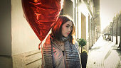 portrait of young woman holding a red balloon on the street