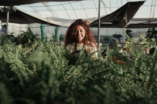 Portrait of a happy young woman with curly hair smiling at camera while working in a greenhouse