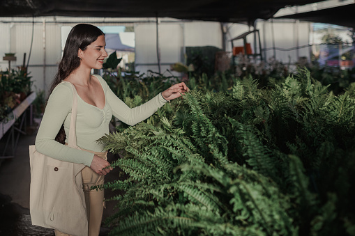 Smiling woman choosing plants to buy in a greenhouse