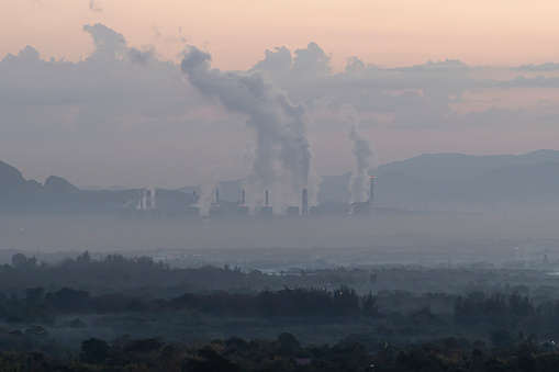 A factory emits smoke from its stacks, and Air pollution over the coal power plant Mae Moh Lampang in the morning with fog, Suitable for industrial and environmental themes