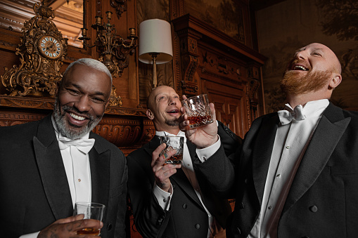 Three handsome 1920s style gentlemen wearing white tie and top hat in a luxury brown bar in a stately home