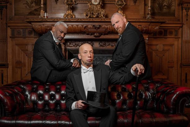 Three handsome 1920s style gentlemen wearing white tie and top hat in a luxury brown bar in a stately home