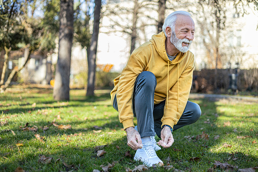 Senior active man tying shoelaces on sports sneakers in park