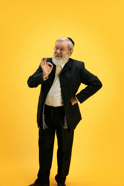 portret uśmiechniętego dojrzałego mężczyzny w garniturze i czarnej jarmułce wykonującego pozytywny gest dłoni na słonecznym żółtym tle. wesołego purim. - judaism jewish ethnicity hasidism rabbi zdjęcia i obrazy z banku zdjęć