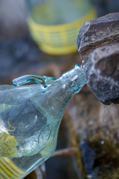 Glass bottle being emptied. Water flowing from almost empty bottle on blue background.