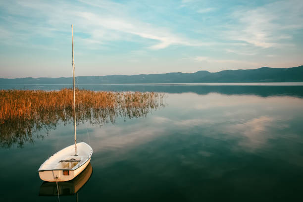 tiny sail boat on a calm lake blue sky feather clouds sunset landscape