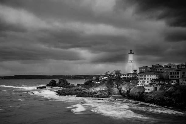 Lighthouse on top of hill in small village rock formations cloudy weather big waves