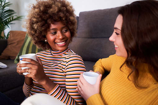 Close up of two woman talking in the living room drinking coffee and talking cheerfully in the morning.