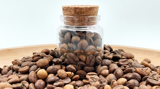 Coffee beans in a small glass jar with a cork lid on the table. Coffee beans packed in a transparent, airtight storage container. Coffee seeds inside a glass jar