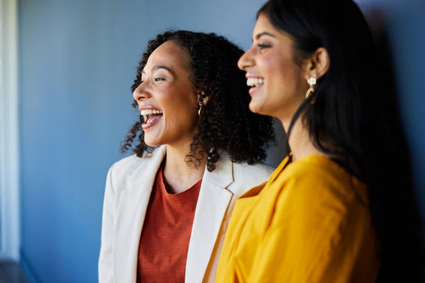 istock Two diverse businesswomen laughing while standing by an office wall 1977304978