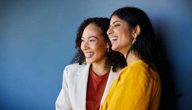 Two diverse businesswomen laughing together by an office wall