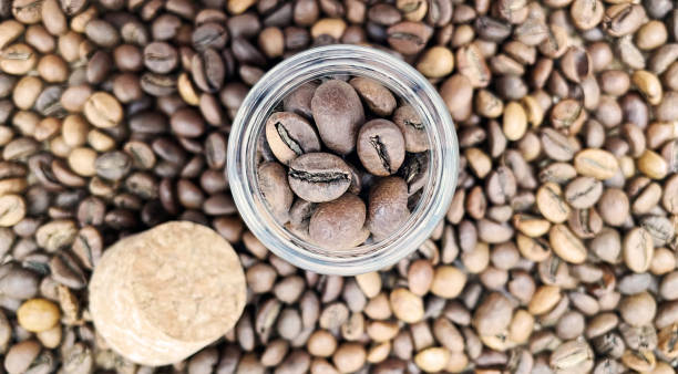 istock Coffee beans in a small glass jar with a cork lid on the table. Coffee beans packed in a transparent, airtight storage container. Coffee seeds inside a glass jar. Flat layout. 1977307086