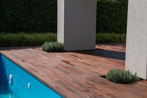 Poolside decking wood floor with greenery, scrub and white pillars