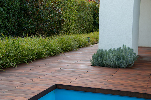 Pool deck wood floor with evergreen fence scrub, grass and white pillar, poolside privacy idea