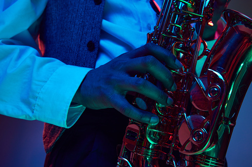 African-American artist, solo performer plays chords on fingering of saxophone, wind instrument in neon light against studio background. Concept of classical musical instrument, concert, festival. Ad