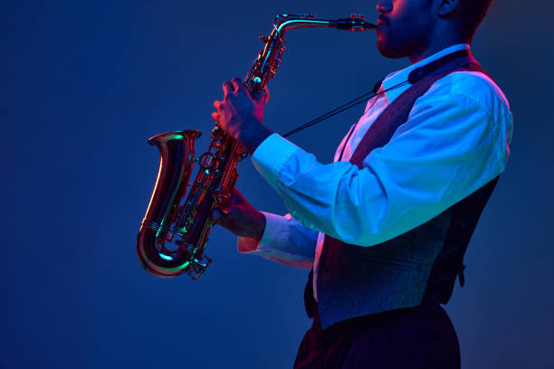 African-American jazz musician playing saxophone his major melodies against blue background in mixed pink-purple lighting. African-American jazz musician playing saxophone his major melodies against blue background in mixed pink-purple lighting. Concept of classical musical instrument, concerts and festivals. Ad sax arts and crafts stock pictures, royalty-free photos & images