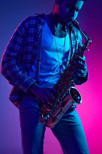 Virtuoso saxophonist, African American man, talented artist playing melody against gradient blue-pink background. Concept of jazz, blues, classy instrumental music, festivals and concerts. Ad