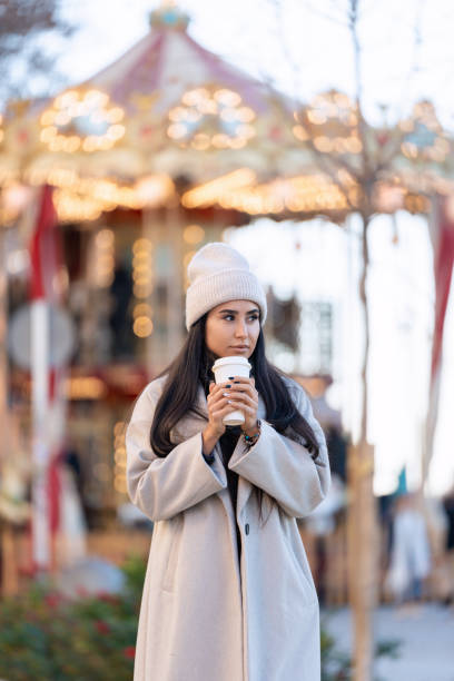 istock Woman with coffee gazing at carousel lights 1977343291