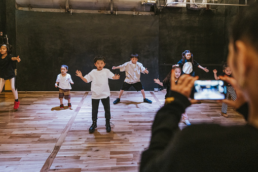 Hip hop dance teacher records the lively performance of Japanese kids, preserving the vibrant essence of their dance in a social media videoclip