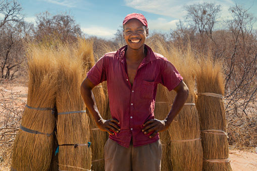 african man standing in front of a stack with dry thatch to sell for roofs, entrepreneur on the side of the road in the bush