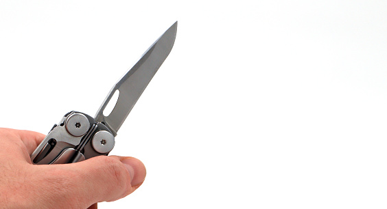 On a white background, a man's hand holds a steel multi-tool with an open knife blade. Pocket folding knife. Portable multi-tasking multi-tool with many tools. EDC concept. Tool for daily practice