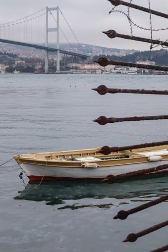 wooden boat shot through fence spiers against the backdrop of the Istanbul bridge and cityscape on a cloudy day