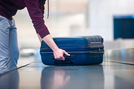 Passenger traveling by plane picking up blue suitcase from conveyor belt in airport arrivals terminal.