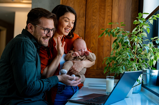 Young happy man and woman holding newborn cute babe dressed in white unisex clothing.