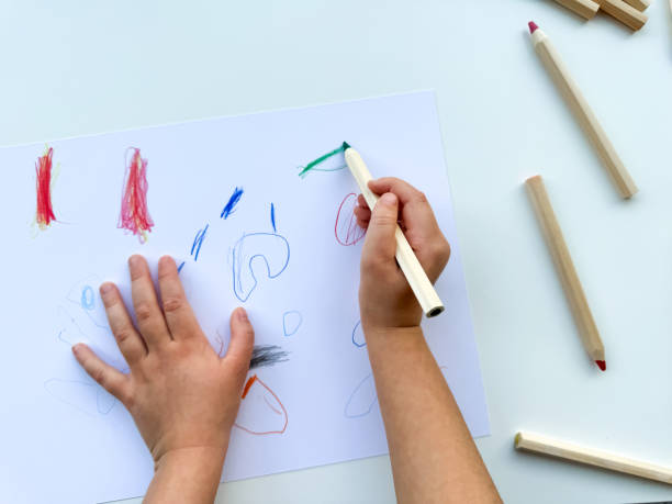 istock small child draws with colored pencils on paper on white table. 1977404663