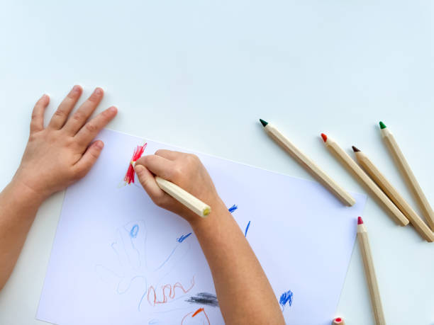 istock small child draws with colored pencils on paper on white table. 1977404664