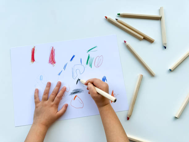 istock small child draws with colored pencils on paper on white table. 1977404671