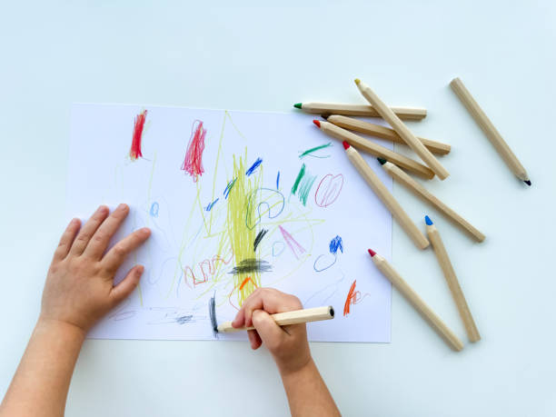 istock small child draws with colored pencils on paper on white table. 1977404674