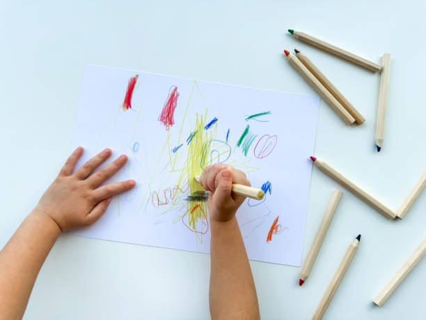 istock small child draws with colored pencils on paper on white table. 1977404678