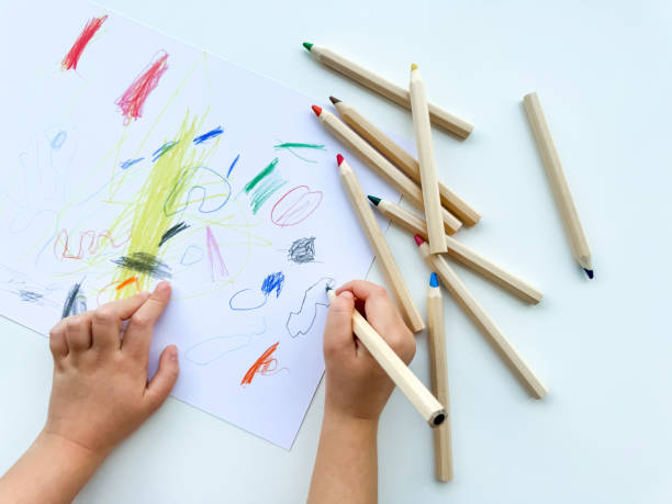 istock small child draws with colored pencils on paper on white table. 1977405197