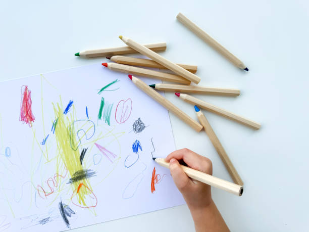 istock small child draws with colored pencils on paper on white table. 1977405203