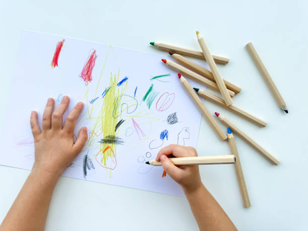 istock small child draws with colored pencils on paper on white table. 1977405204