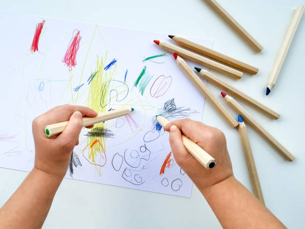 istock small child draws with colored pencils on paper on white table. 1977405242