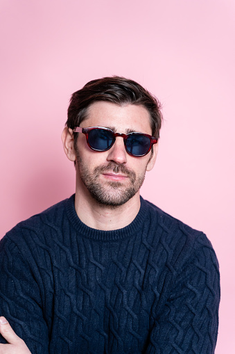 Thoughtful man in dark sweater and red sunglasses, pink background