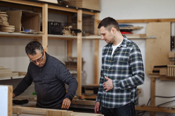 istock Craftsman measuring wooden plank and student learning working techniques. 1977418991