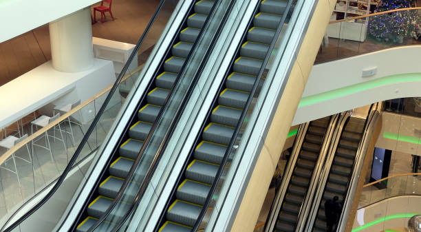 istock Escalator in a large multi-storey shopping center. High angle view. Going up and down an escalator with glass walls and metal steps in a sparsely populated business center. 1977419685