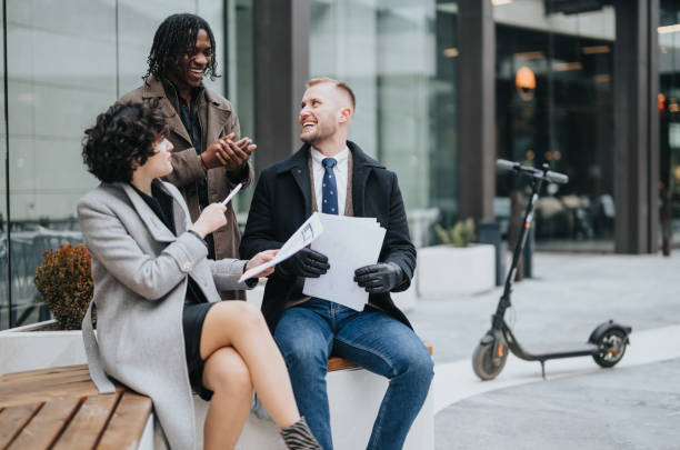 istock Three multiracial business people happily engaging in a conversation outdoors on a bench, with documents in hand and an electric scooter nearby. 1977424105