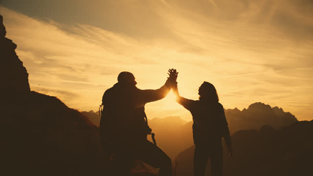 SLO MO Embracing the Summit: Silhouettes of a Couple in a Heartfelt Gesture of Support on Mountain Trails at Sunset