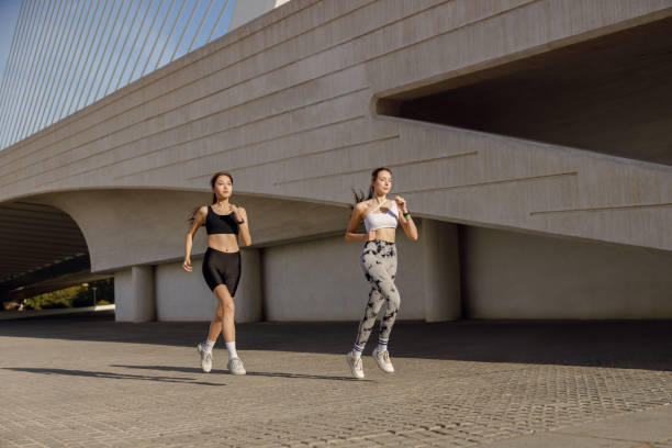 istock Two active women athlete running on sunny morning side by side on modern buildings background 1977427493