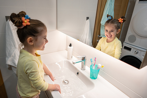 Caucasian toddler girl observing herself in the bathroom mirror, while maintaining her hygiene