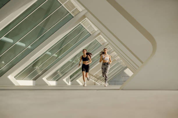 istock Two active women athlete running on sunny morning side by side on modern buildings background 1977437145