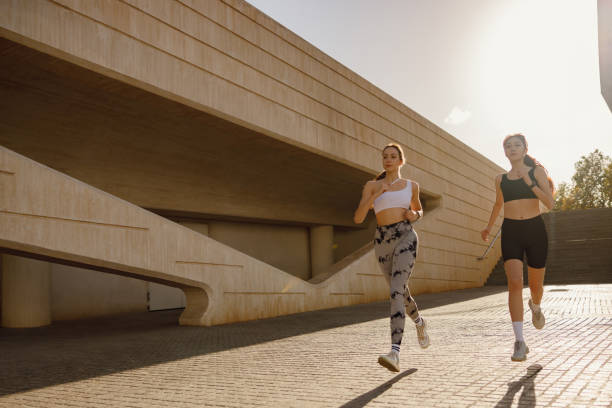 istock Two active women athlete running on sunny morning side by side on modern buildings background 1977442496