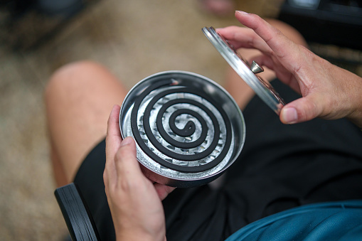 Close up image of an adult is depicted preparing a mosquito repellent coil at a campsite, emphasizing the necessary measures taken to ensure a comfortable outdoor experience.