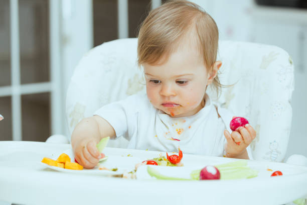 Vegetarian child, trying healthy food lunch time at home baby led weaning. stock photo