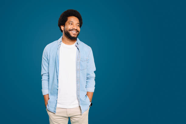 istock A friendly man with a curly afro smiles casually, hands in pockets against a cool blue background 1977506246